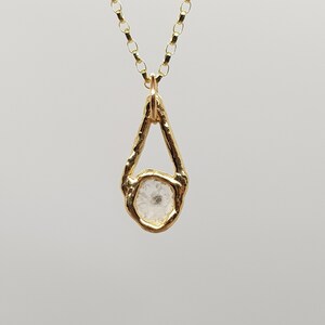 May include: A gold necklace with a teardrop-shaped pendant featuring a clear crystal stone set in a gold frame.