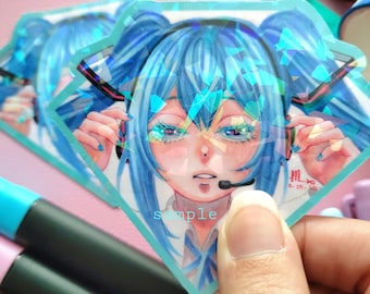 May include: Diamond-shaped sticker featuring a blue-haired anime character with a headset and microphone. The sticker has a holographic effect and the word "sample" is printed on it. The art is signed "MINAKINNA".