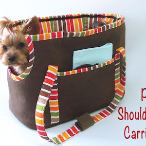 May include: A brown pet carrier with a striped fabric lining and a shoulder strap. The carrier has a pocket on the front and a small dog is peeking out of the top.