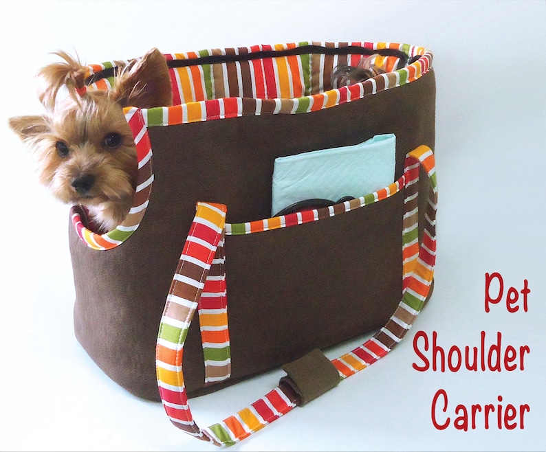 May include: A brown pet carrier with a striped fabric lining and a shoulder strap. The carrier has a pocket on the front and a small dog is peeking out of the top.