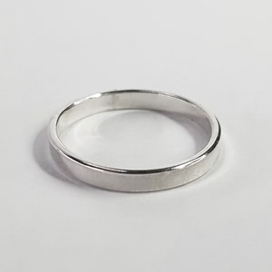 Könnte beinhalten: Ein polierter silberfarbener Ring mit einem glatten, flachen Band und einer kreisförmigen Form. Die Metalloberfläche ist reflektierend und farblich einheitlich und zeigt ein einfaches, durchgehendes Design ohne Gravuren oder Steine.