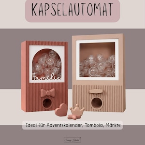 Könnte beinhalten: Zwei vertikale, rechteckige Kapselautomaten mit gerippter Textur. Der linke ist terrakottafarben mit einer Schleife und dem Schriftzug "Familie" auf dem Glas. Der rechte ist beige. Beide enthalten durchsichtige Kunststoffkugeln und kleine Dekofiguren.