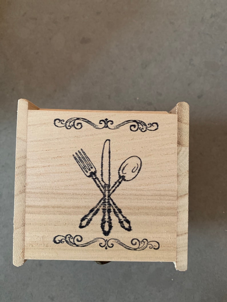 Puede incluir: Una caja de madera con un dise&ntilde;o decorativo de un tenedor, cuchillo y cuchara. La caja tiene un acabado de madera clara y un dise&ntilde;o negro.