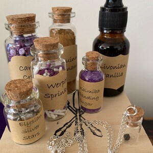 Puede incluir: Una colecci&oacute;n de peque&ntilde;as botellas de vidrio con tapas de corcho, llenas de diversos art&iacute;culos, incluyendo purpurina morada y blanca, estrellas plateadas y purpurina morada. Las botellas est&aacute;n etiquetadas con nombres como "Werpo Sprink", "Kalimba Sanding Sugar" y "Elysian Silver Stars". Tambi&eacute;n hay una botella de l&iacute;quido oscuro etiquetada como "Livonian Vanilla" y un collar de cadena plateada con un peque&ntilde;o colgante de botella de vidrio.