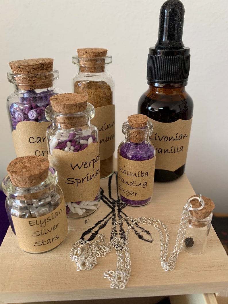 Puede incluir: Una colecci&oacute;n de peque&ntilde;as botellas de vidrio con tapas de corcho, llenas de diversos art&iacute;culos, incluyendo purpurina morada y blanca, estrellas plateadas y purpurina morada. Las botellas est&aacute;n etiquetadas con nombres como "Werpo Sprink", "Kalimba Sanding Sugar" y "Elysian Silver Stars". Tambi&eacute;n hay una botella de l&iacute;quido oscuro etiquetada como "Livonian Vanilla" y un collar de cadena plateada con un peque&ntilde;o colgante de botella de vidrio.
