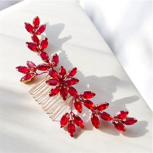 May include: A red crystal hair comb with a floral design. The comb is made of metal and has a gold finish. The crystals are arranged in a cascading pattern, creating a delicate and elegant look.
