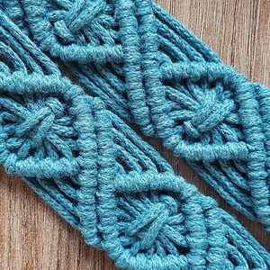 May include: A close-up of a teal blue macrame cord with a diamond pattern. The cord is woven into a decorative design.