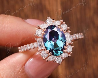 May include: An oval-cut color-changing gemstone ring set in rose gold. The central stone is surrounded by a halo of small round and baguette-cut white stones. The band features a pavé setting with small white stones along the shank.