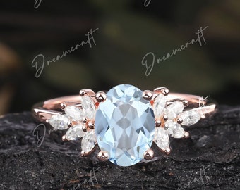 May include: A rose gold engagement ring with a light blue oval-shaped center stone and a halo of smaller diamonds. The ring is set on a dark brown wooden surface.