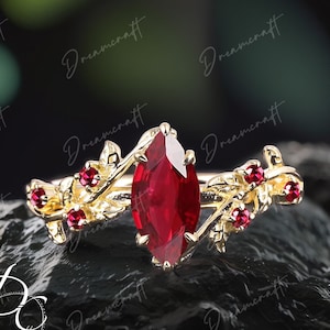 Op de afbeelding: Een gouden ring met een grote, rode, markiesvormige edelsteen omringd door kleinere rode edelstenen en gouden bladontwerpen.