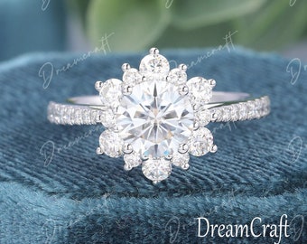May include: A silver engagement ring with a large round center stone surrounded by smaller stones in a flower-like design.