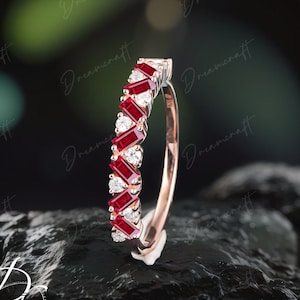 May include: A rose gold band ring with a row of alternating red ruby and clear round diamonds. The ring is set against a dark grey background.