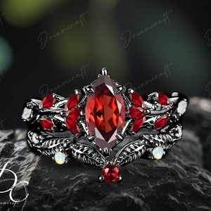 May include: A black ring set with a large red gemstone surrounded by smaller red gemstones and two white opals. The ring features a leaf design.