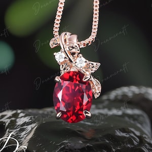 May include: A rose gold necklace with a red gemstone pendant surrounded by small clear gemstones and leaves. The pendant is on a delicate chain.