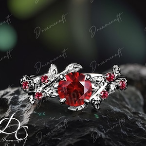 Op de afbeelding: Een zilveren ring met een grote rode edelsteen omringd door kleinere rode edelstenen en zilveren bladeren.