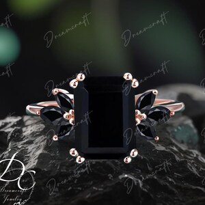 K&ouml;nnte beinhalten: Ein Ring aus Ros&eacute;gold mit einem gro&szlig;en, smaragdgeschliffenen schwarzen Mittelstein, der auf jeder Seite von drei markisengeschliffenen schwarzen Seitensteinen flankiert wird. Die Ringschiene ist aus Ros&eacute;gold und hat kleine Krappen.
