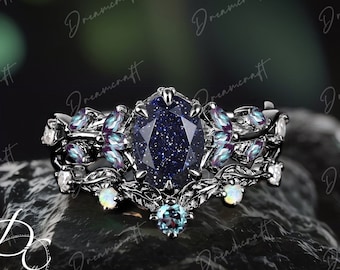 May include: A black ring with a large blue gemstone surrounded by smaller blue and purple gemstones. The ring has a delicate, intricate design with a floral motif.
