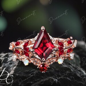 May include: A rose gold ring featuring a large, square-shaped red gemstone surrounded by smaller red gemstones and white opals. The ring has a delicate, leafy design.