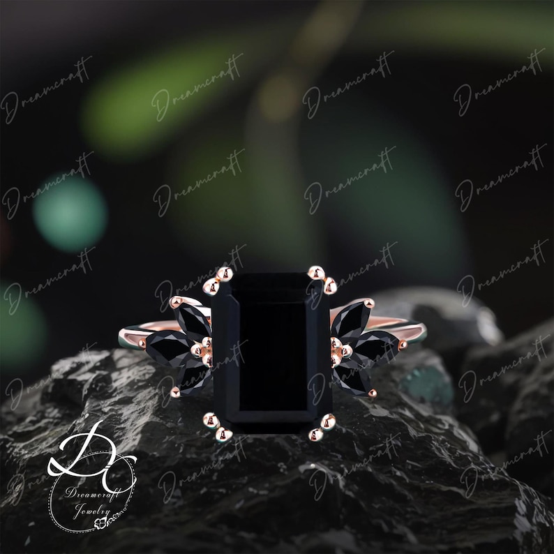 K&ouml;nnte beinhalten: Ein Ring aus Ros&eacute;gold mit einem gro&szlig;en, smaragdgeschliffenen schwarzen Mittelstein, der auf jeder Seite von drei markisengeschliffenen schwarzen Seitensteinen flankiert wird. Die Ringschiene ist aus Ros&eacute;gold und hat kleine Krappen.