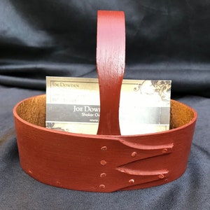 May include: A red wooden basket with a leather handle and a business card inside. The basket has a carved design and metal rivets. The business card reads "Joe Dowden, Shaker Oven, www.joedowden.com".