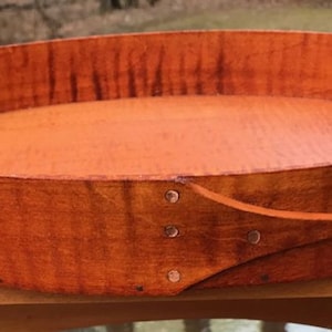 May include: A round wooden tray with a natural wood finish. The tray has a single handle on one side and is made of wood.