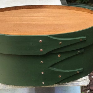May include: A green wooden oval box with a wooden lid and copper colored metal accents. The box has two hinged lids with decorative cutouts.