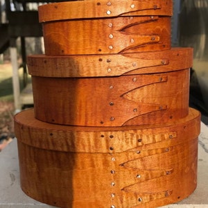 May include: Three wooden nesting boxes with a natural wood finish and copper tacks. The boxes are stacked on top of each other, with the largest box on the bottom and the smallest box on top.
