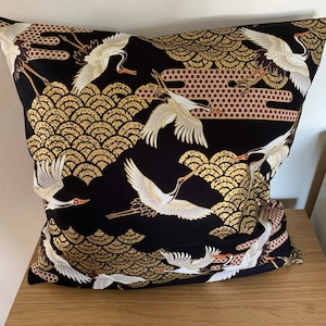 May include: Black throw pillow with a gold and white crane pattern. The cranes are flying against a background of gold and black scales.