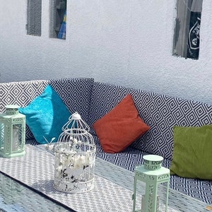 Puede incluir: Sofá seccional de exterior con cojines estampados geométricos grises y blancos y cojines decorativos coloridos. Los cojines son rosas, turquesas, naranjas, verdes y morados. Faroles decorativos y una mesa con tapa de cristal.