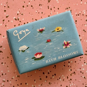 May include: A light blue box with the word "Goya" in white script. The box is decorated with illustrations of various colourful water lilies and the words "BATH BLOSSOMS".
