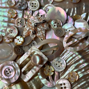 May include: A collection of iridescent mother-of-pearl buttons and buckles in various shapes and sizes. The assortment includes round, oval, and rectangular pieces with two or four holes, featuring natural pearlescent tones and textures.