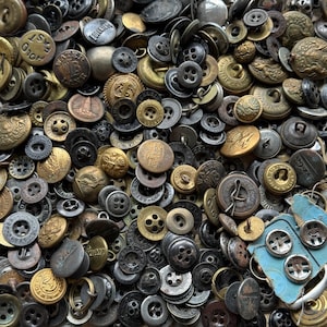 May include: A large collection of assorted metal buttons in various shades of gold, bronze, silver, and black. The buttons feature diverse designs, including embossed text, intricate patterns, and classic four-hole styles, with some attached to a blue card.
