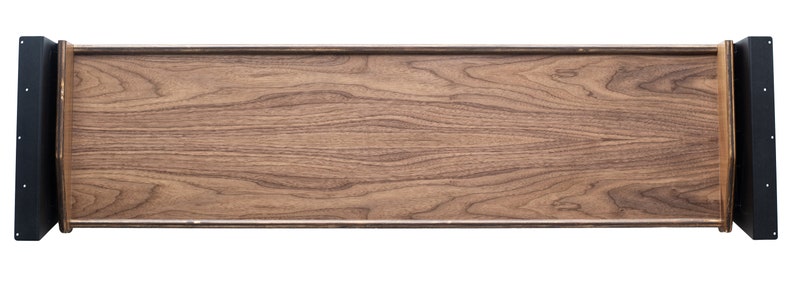 May include: A long, rectangular wooden tray with black metal end pieces. The tray has a natural wood finish and a smooth surface.