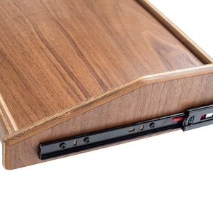 May include: Close-up of a wooden drawer slide with black metal rails and a red plastic release button. The drawer slide is attached to a wooden drawer with a beveled edge.
