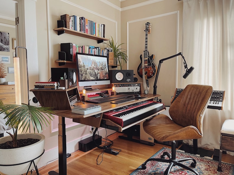 May include: A home music studio with a wooden desk, a computer, a keyboard, a microphone, a guitar, and a brown leather office chair.