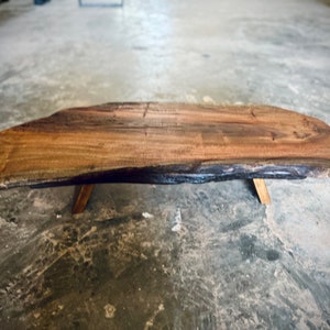 May include: A large, natural wood coffee table with a live edge top and a dark brown stain. The table has four simple, wooden legs.