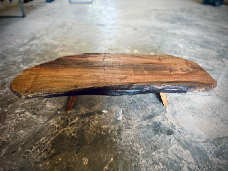 May include: A large, natural wood coffee table with a live edge top and a dark brown stain. The table has four simple, wooden legs.