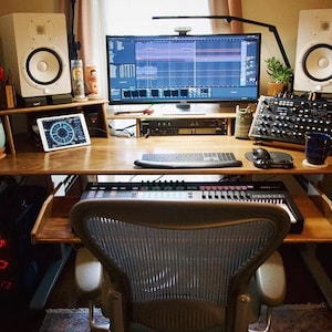 May include: A home music studio setup with a wooden desk, a computer monitor, a keyboard, a pair of white studio monitors, a synthesizer, and a microphone.