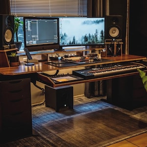 May include: A wooden desk with a black keyboard, a black and white computer monitor, a black speaker, and a black and white keyboard. The desk is lit with a blue light.