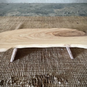 May include: A natural wood serving tray with a live edge and two small wooden legs. The tray is light brown in color and has a smooth, polished finish.