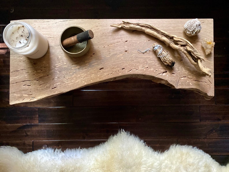 May include: A wooden table top with a candle, a singing bowl, a piece of driftwood, a bundle of sage, and a crystal. The table top is light brown with a natural wood grain.