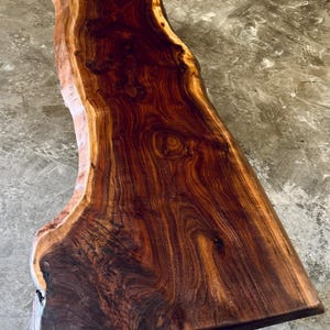 May include: A large, live edge slab of wood with a rich, dark brown color and a natural, wavy grain pattern. The wood has a smooth, polished finish.