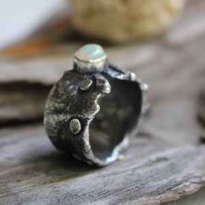 May include: A silver ring with a textured, organic design. The ring features a white opal gemstone set in the center.