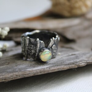 May include: A silver ring with a textured, organic design and a round, white opal gemstone.