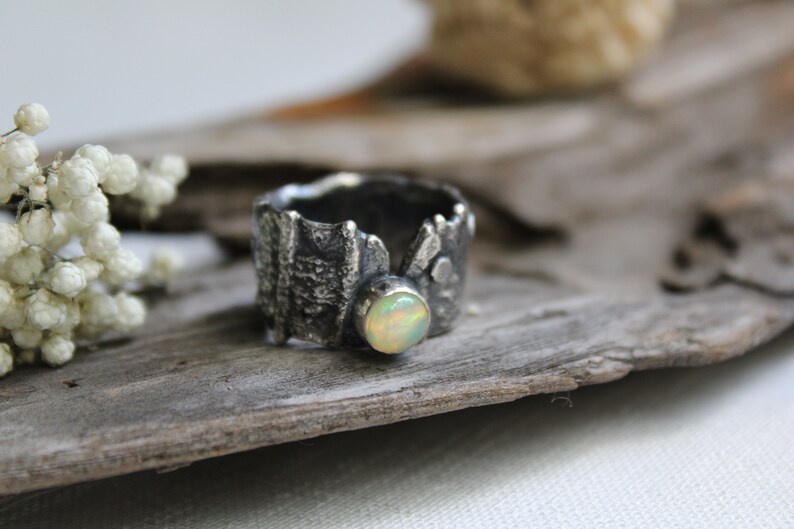 May include: A silver ring with a textured, organic design and a round, white opal gemstone.