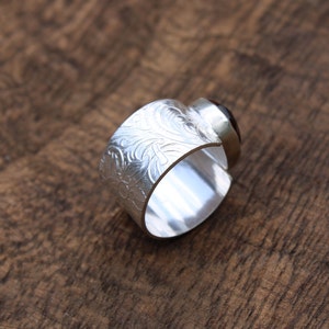 May include: A silver ring with an ornate engraved design and a dark brown gemstone.