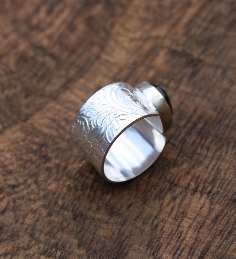 May include: A silver ring with an ornate engraved design and a dark brown gemstone.