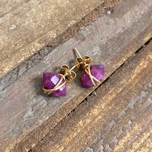 May include: A pair of gold earrings with a purple gemstone set in a wire cage design.