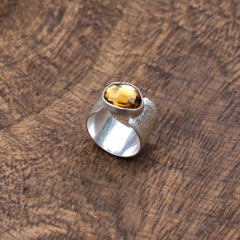 May include: A silver ring with a textured band and a large, faceted, amber-colored gemstone.