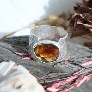 May include: A silver ring with an intricate design and a large, faceted, amber-colored gemstone.